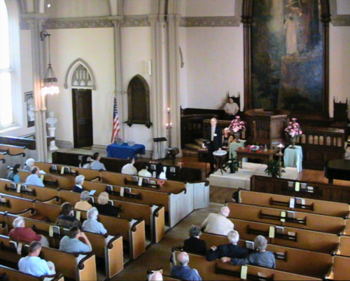 Interior of the old stone church of First Unitarian Church of New Bedford, looking from the organ loft over the ehads of the congregation towards the pulpit and the Tifanny mosaic