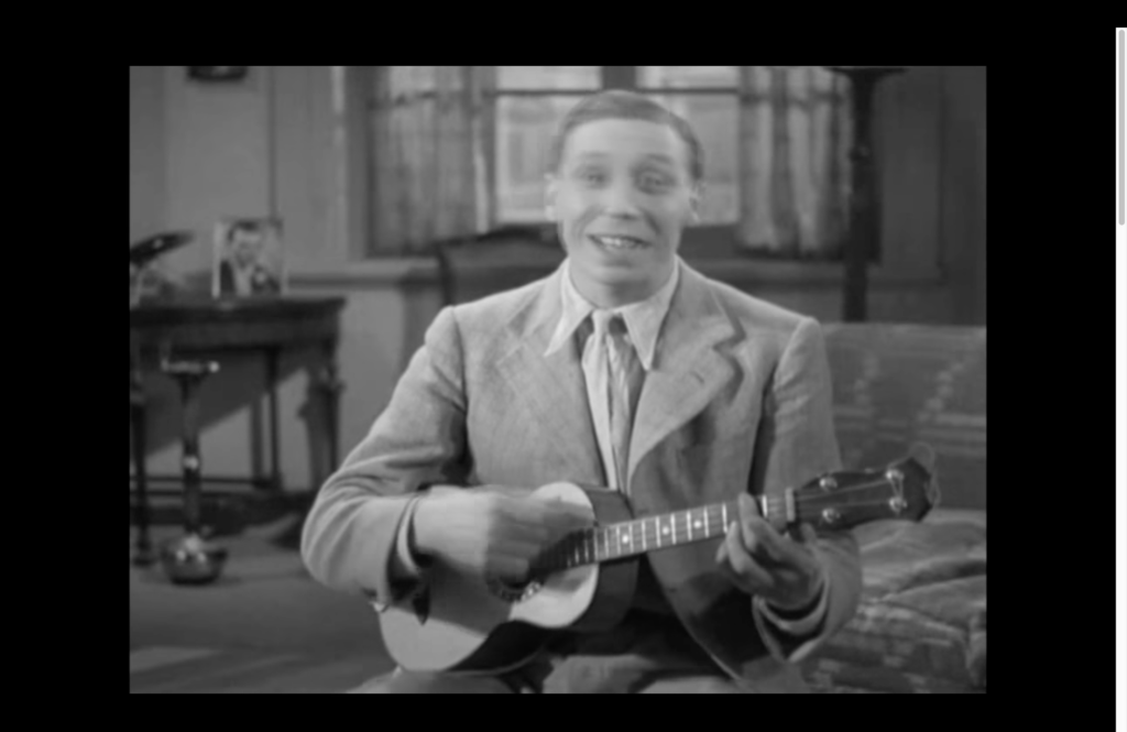 Screen grab from an old film showing a man playing a ukulele.